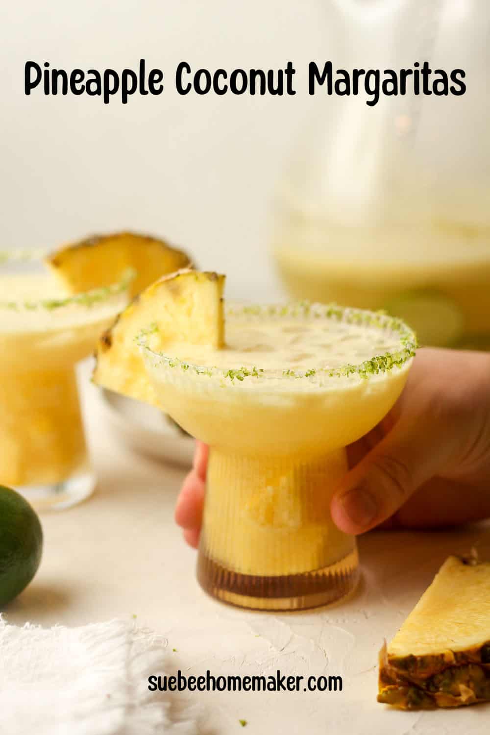 A hand on a pineapple coconut margarita with a lime/salt rim.