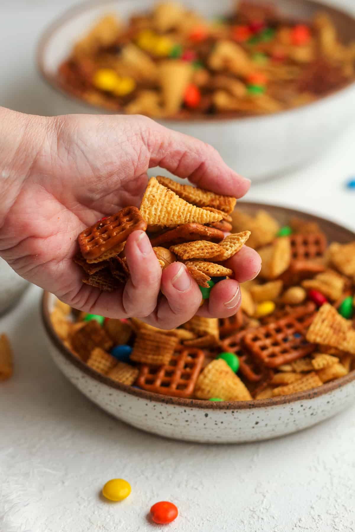 A hand reaching for a bowl of spicy chex mix.