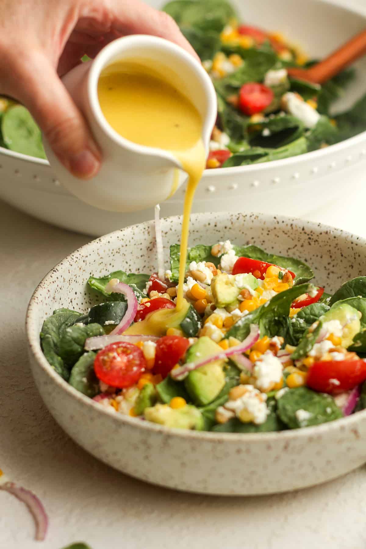 Side view of some creamy salad dressing being poured into a serving of salad.