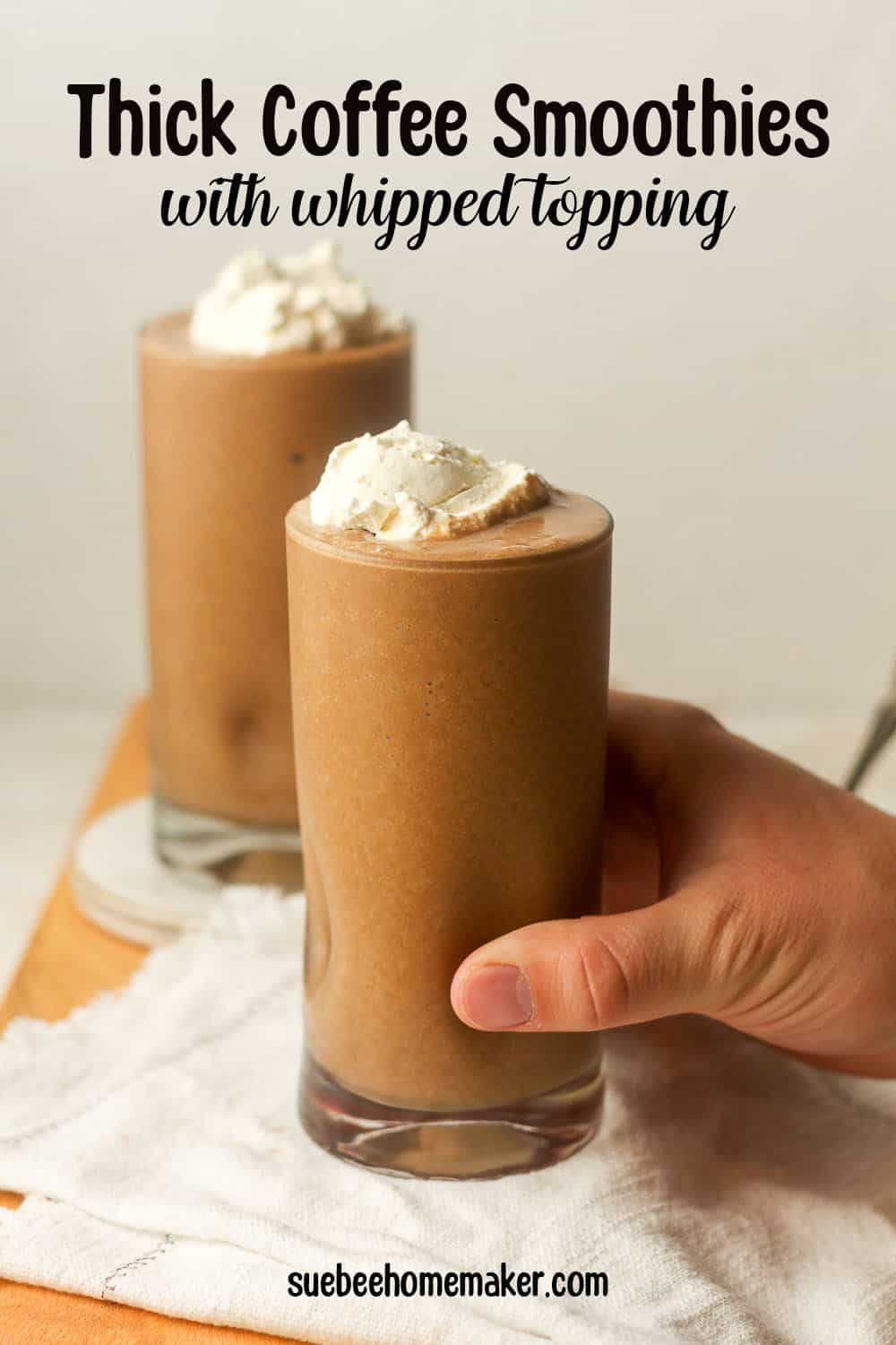 A hand reaching for a thick coffee smoothie with whipped topping.