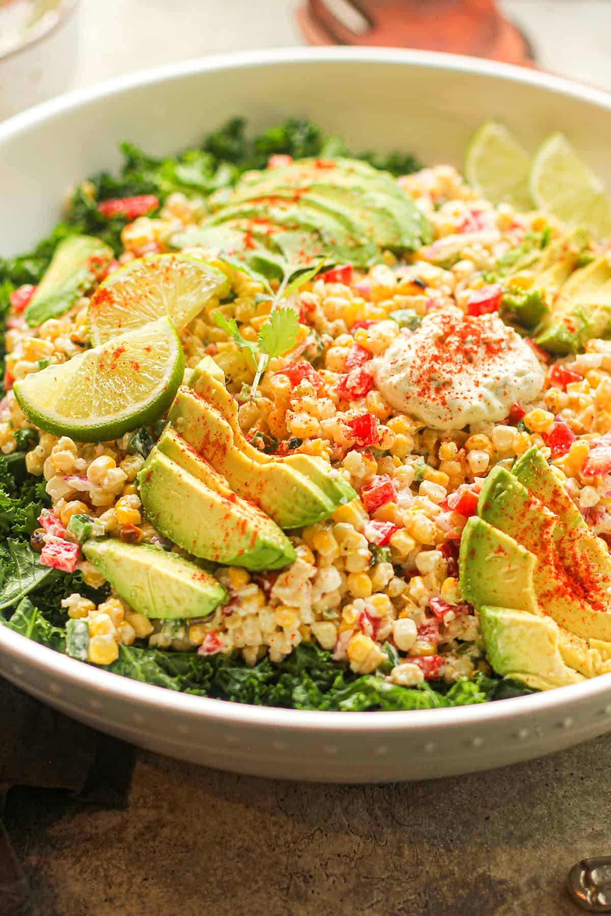 Side view of a large bowl of Mexican street corn kale salad with avocado slices.