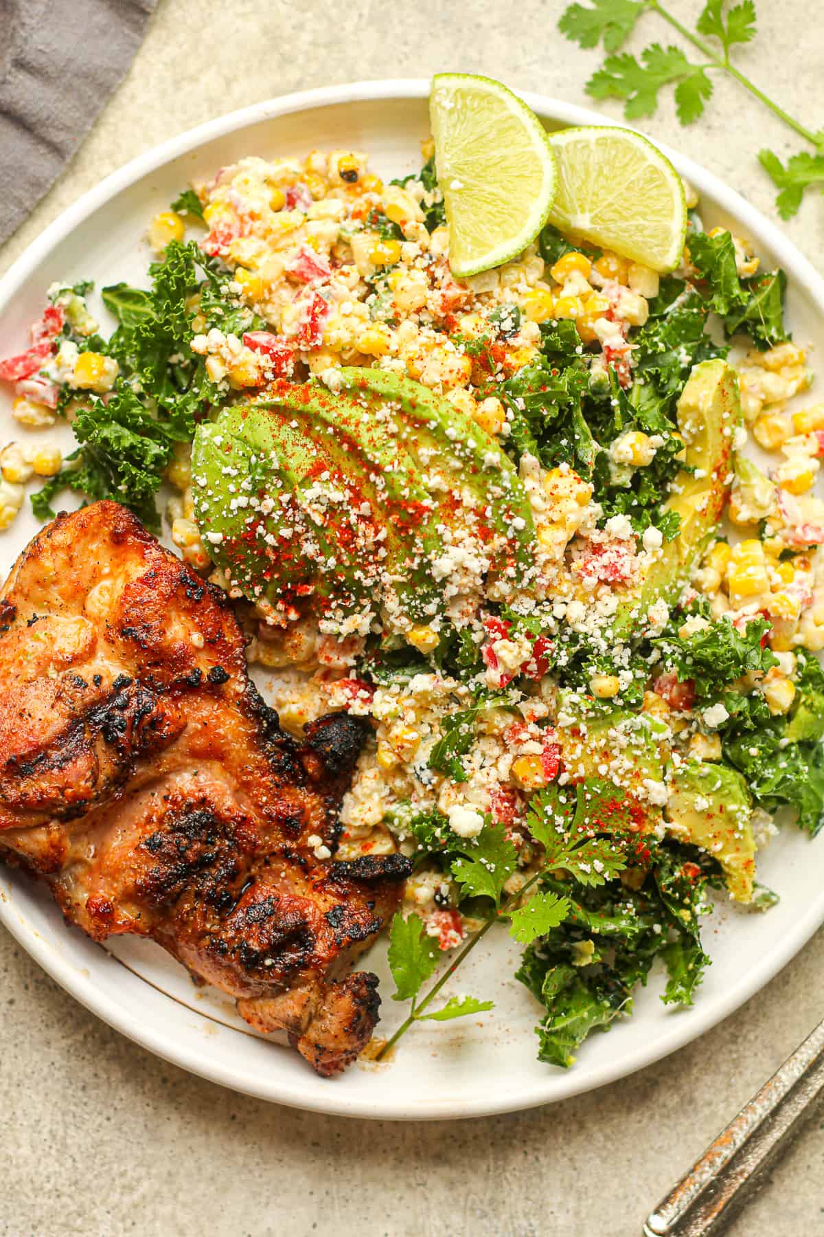 A white plate with Mexican street corn kale salad and a piece of grilled chicken.