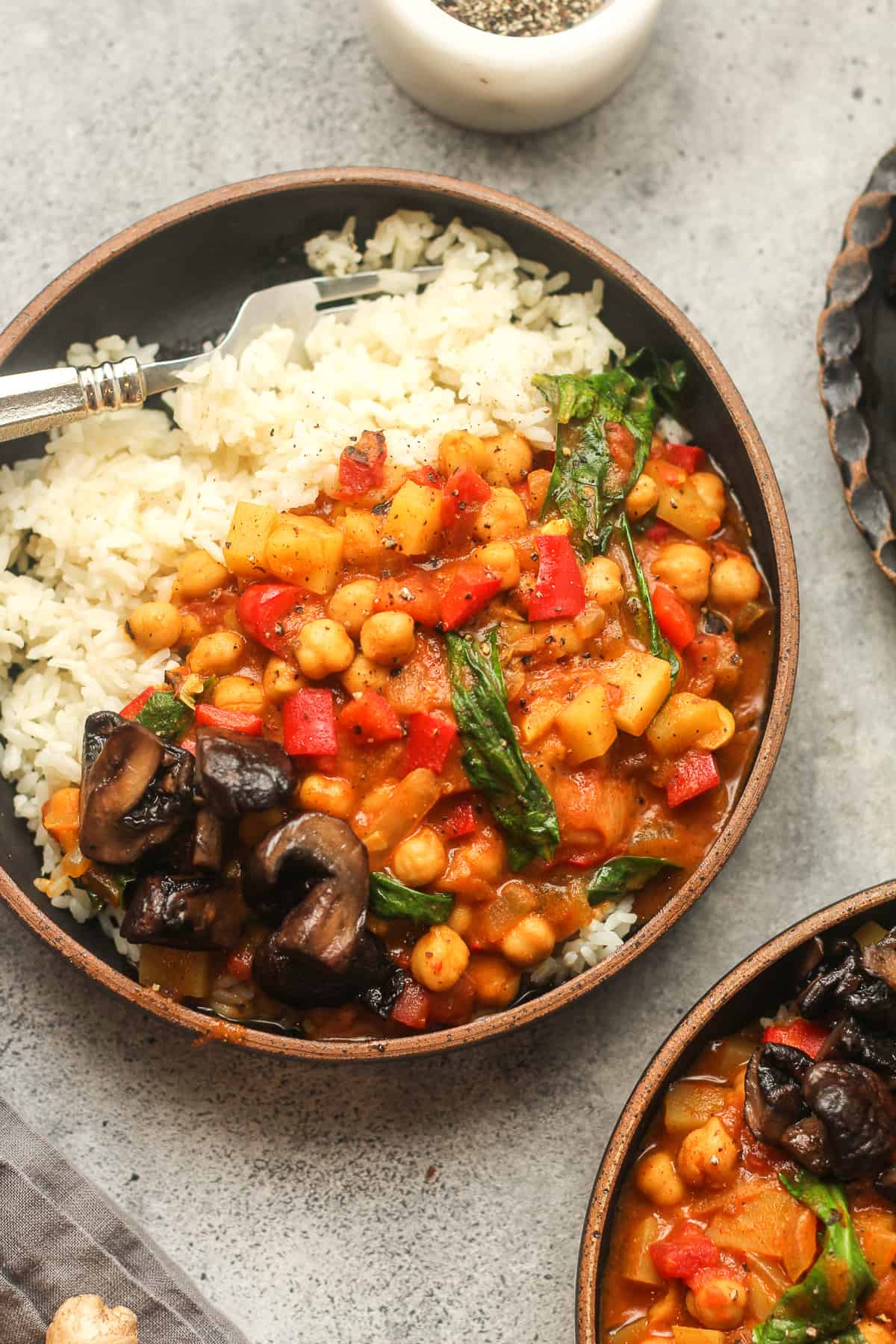 Two black bowls of chickpea and spinach curry over rice.