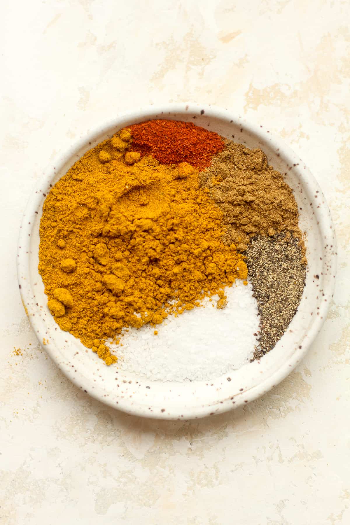 A plate of the seasonings - curry, cumin, cayenne, salt, and pepper.