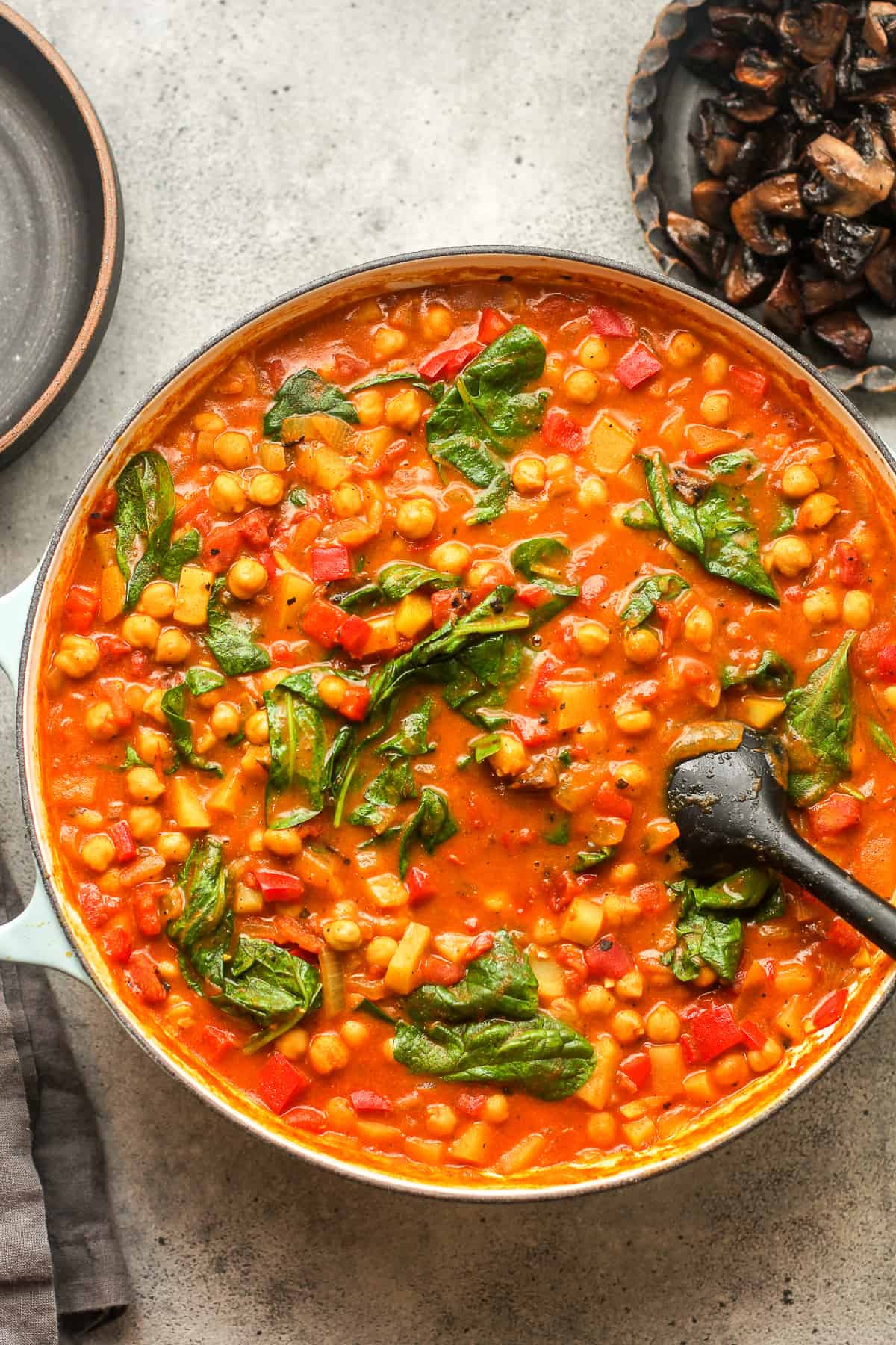 A large shallow pot of spinach and chickpea curry with a spatula.