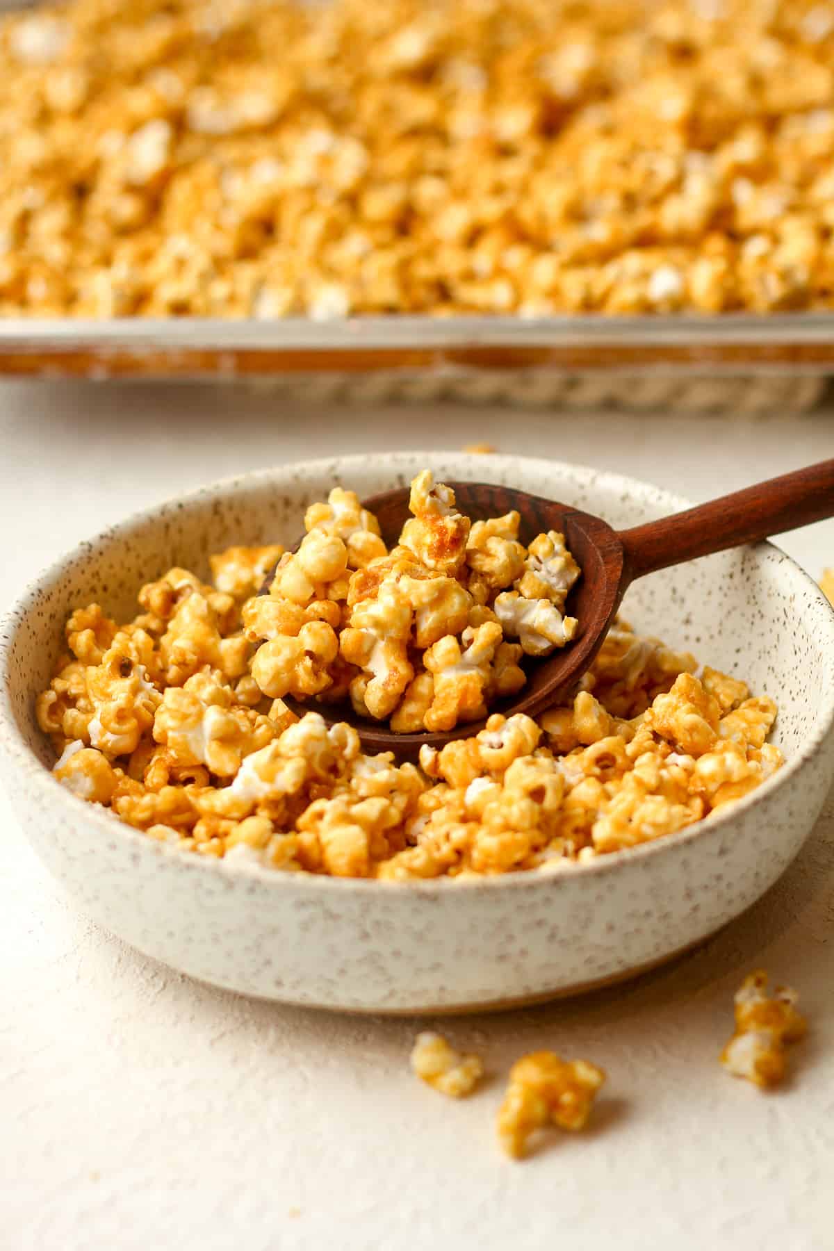 A bowl of caramel popcorn in front of a pan of it.