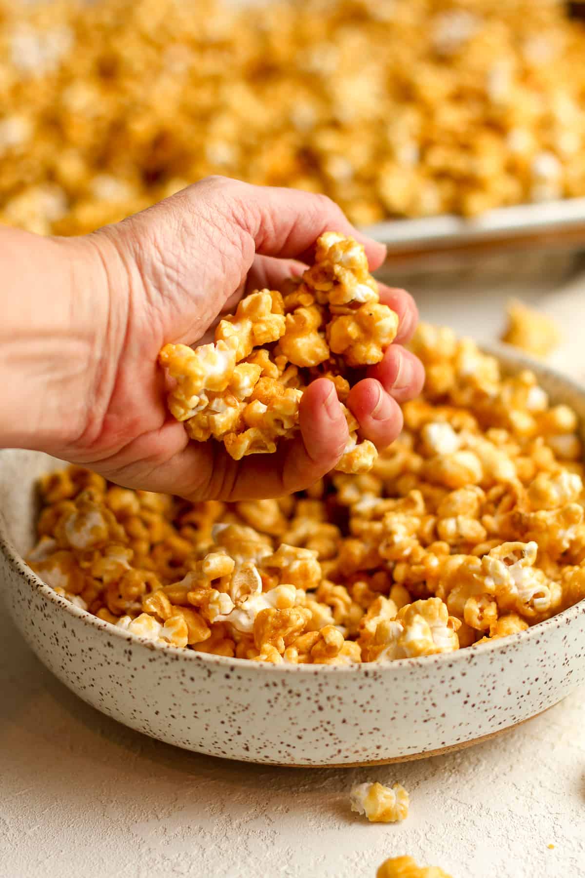 Side view of my hand with some caramel popcorn over a bowl.