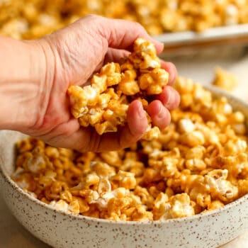 A handful of caramel popcorn over a bowl.