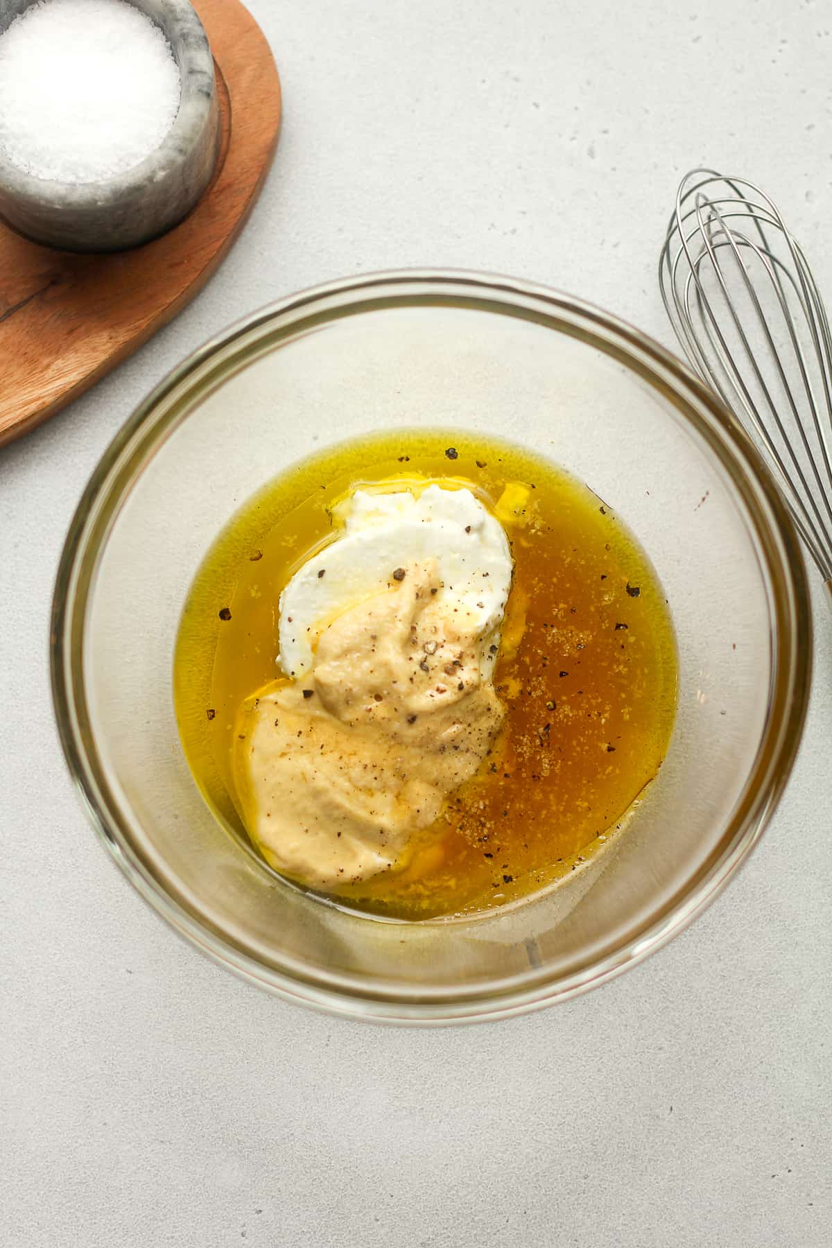 A bowl of the dressing ingredients with a whisk beside it.