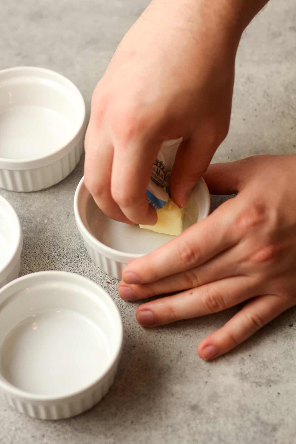 Hands rubbing the butter in the ramekin.