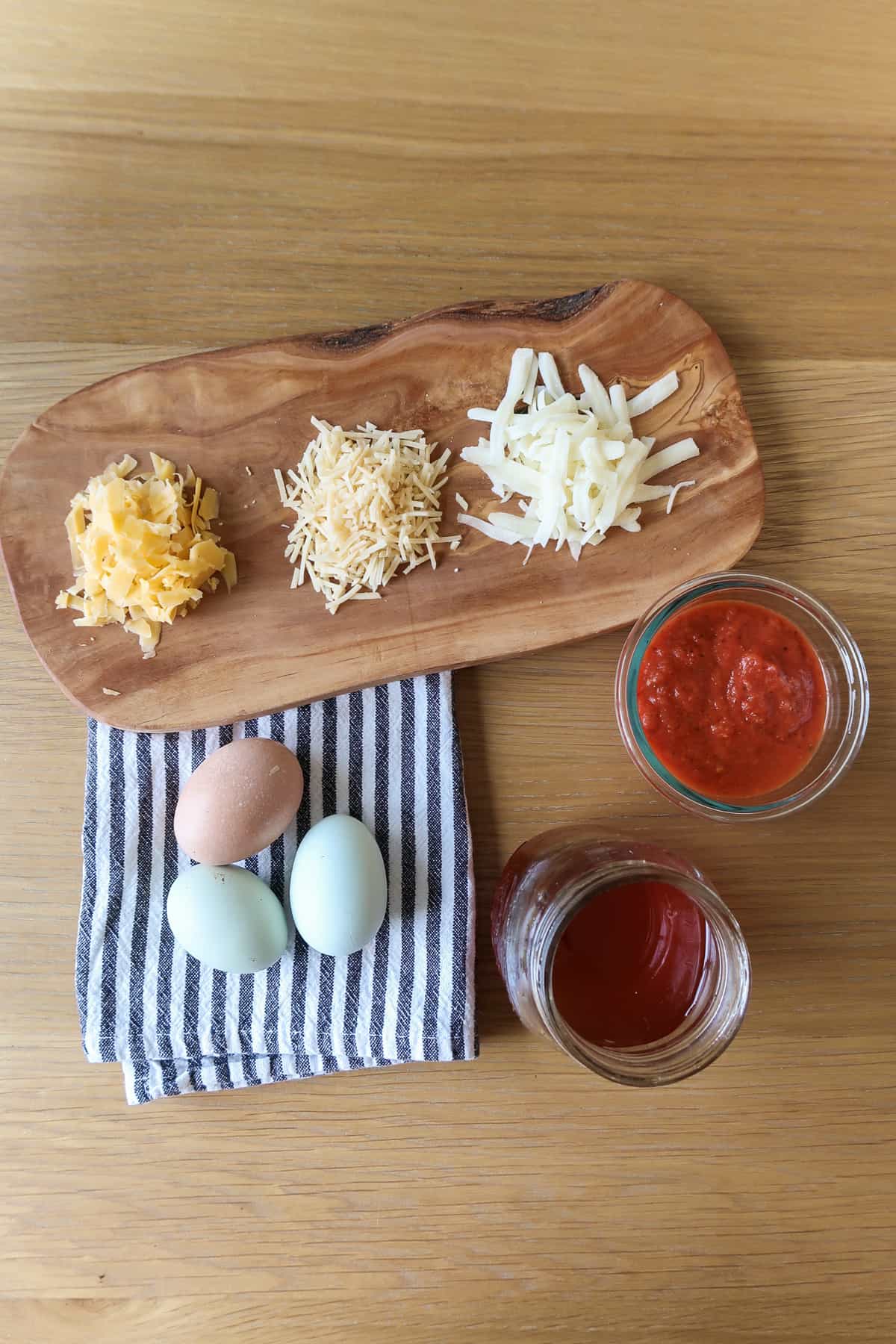 The cheese, eggs, and pizza sauce ingredients on a wood surface.