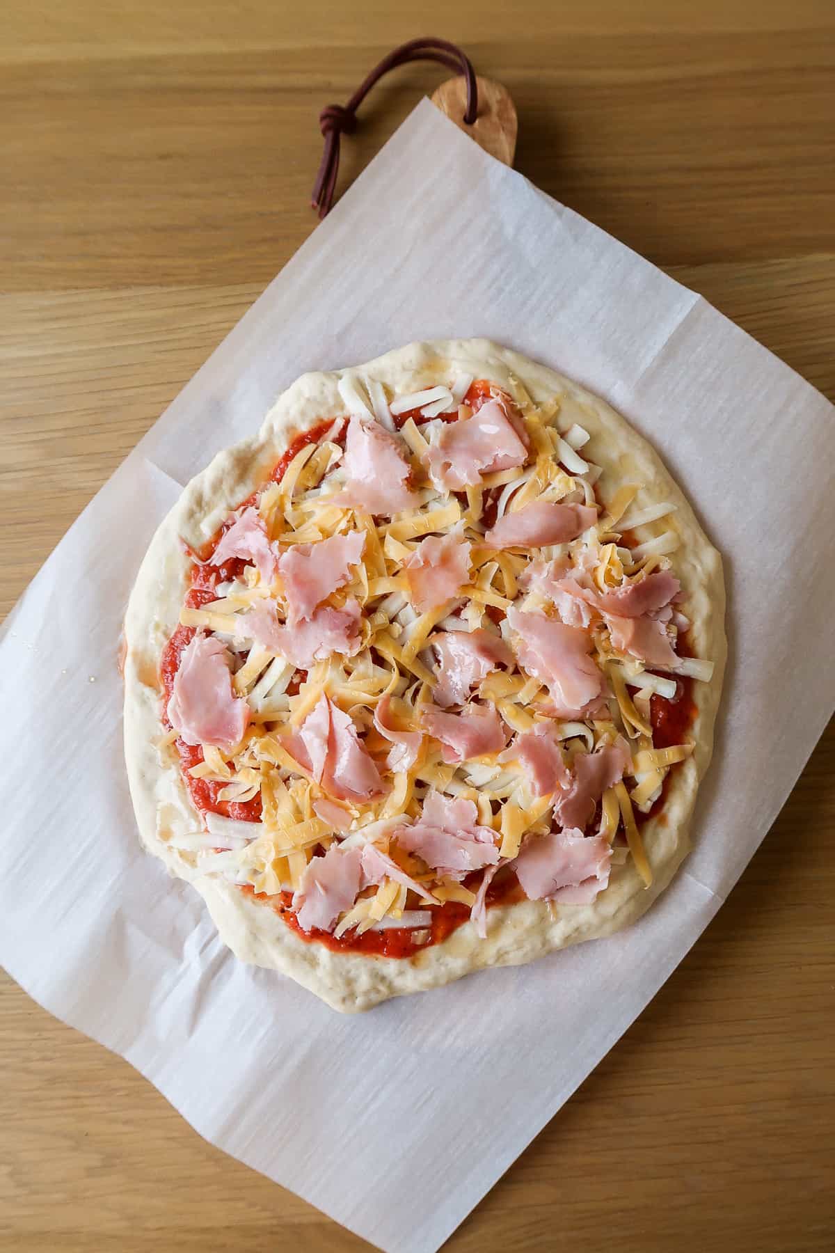 A prepped pizza before grilling it with ham on top.