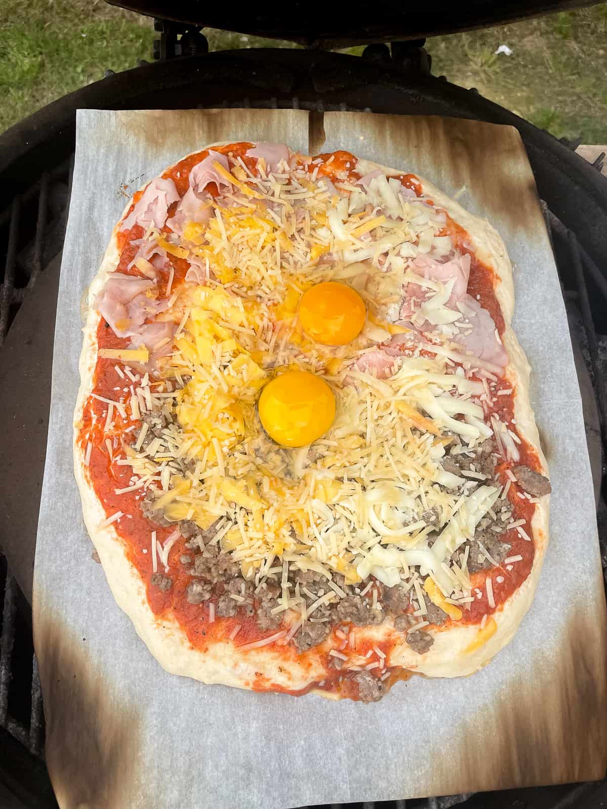 One. of the pizzas on the grill with eggs on top.