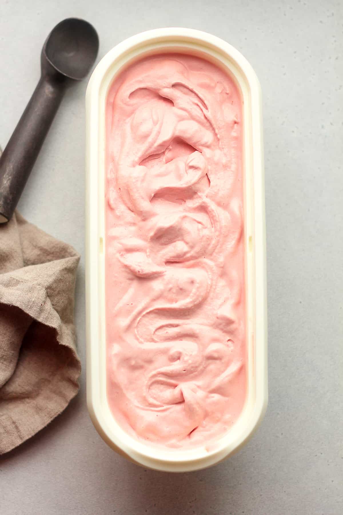 An oblong white container of raspberry ice cream with an ice cream scoop next to it