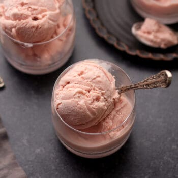 Overhead view of three glass bowls of raspberry ice cream on a black surface.