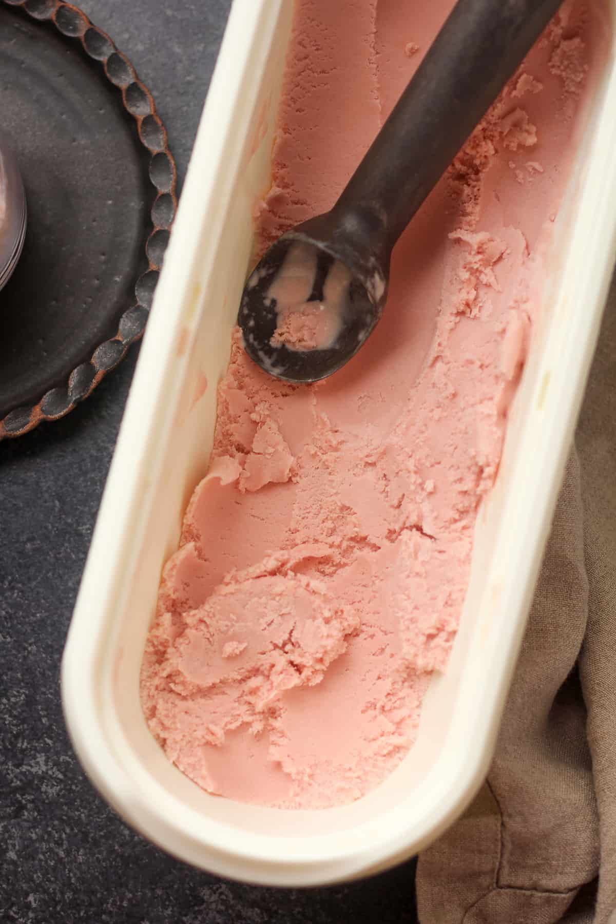Overhead view of an oblong container of ice cream with an ice cream scoop.