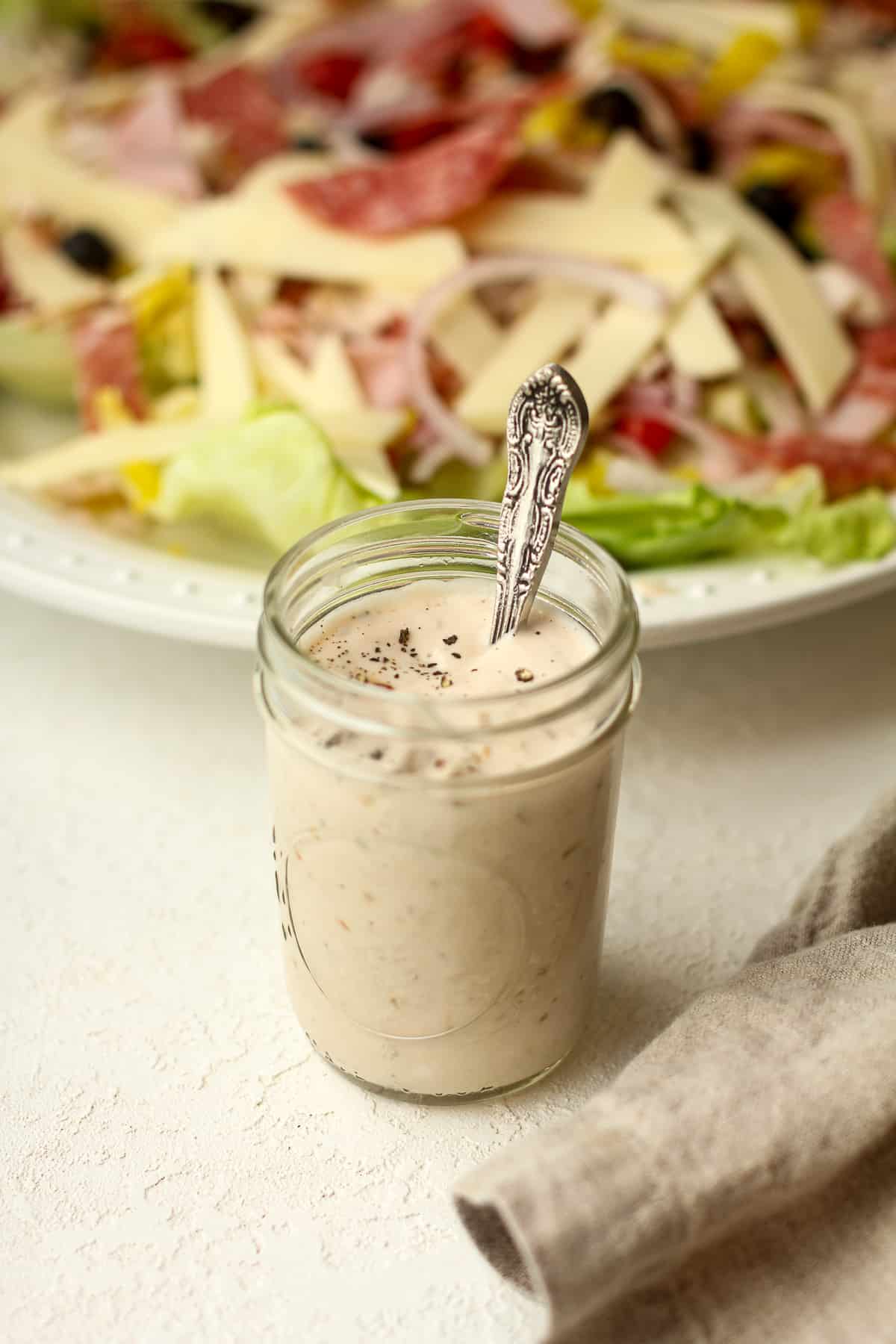 Side view of a jar of dressing in front of a platter of grinder salad.
