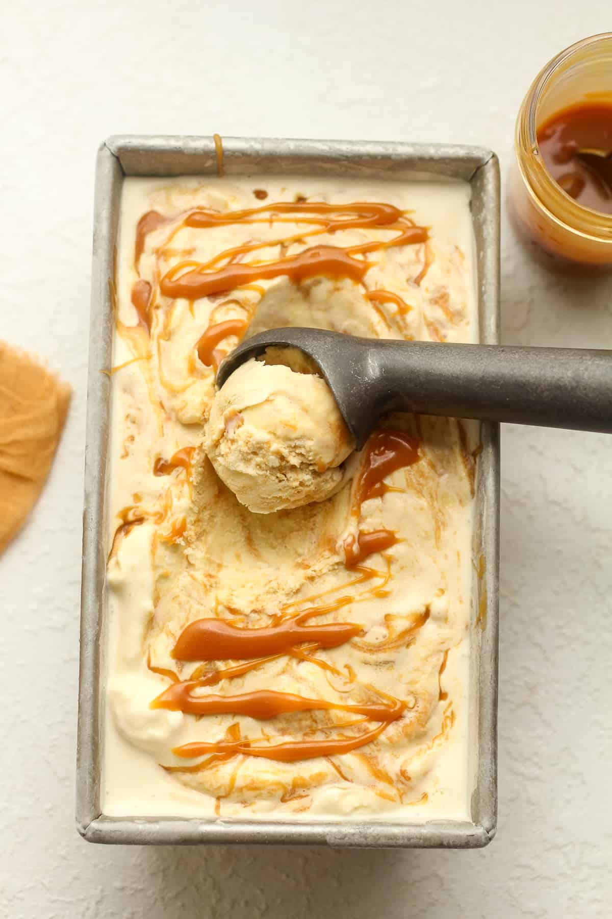 Overhead view of a pan of caramel ice cream with a scoop scooping it up.