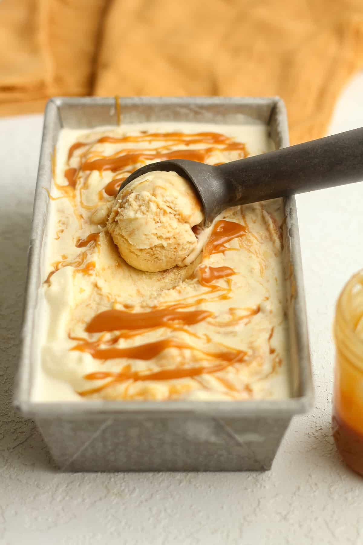 Side view of a pan of caramel swirl ice cream with a scoop inside it.