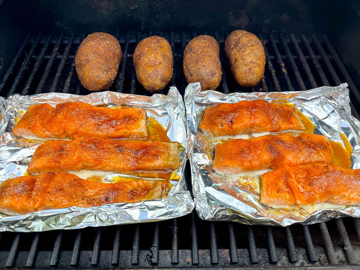 The smoked salmon on tin foil on the grill with four smoked potatoes.