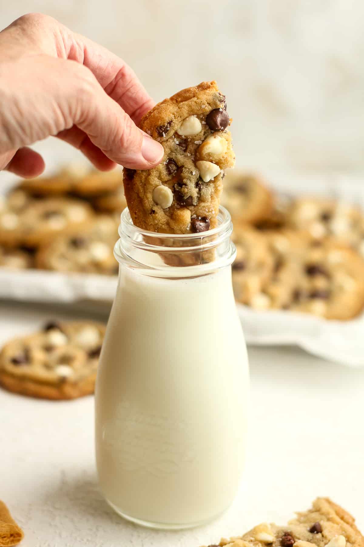 A hand dipping a half cookie into a jar of milk.