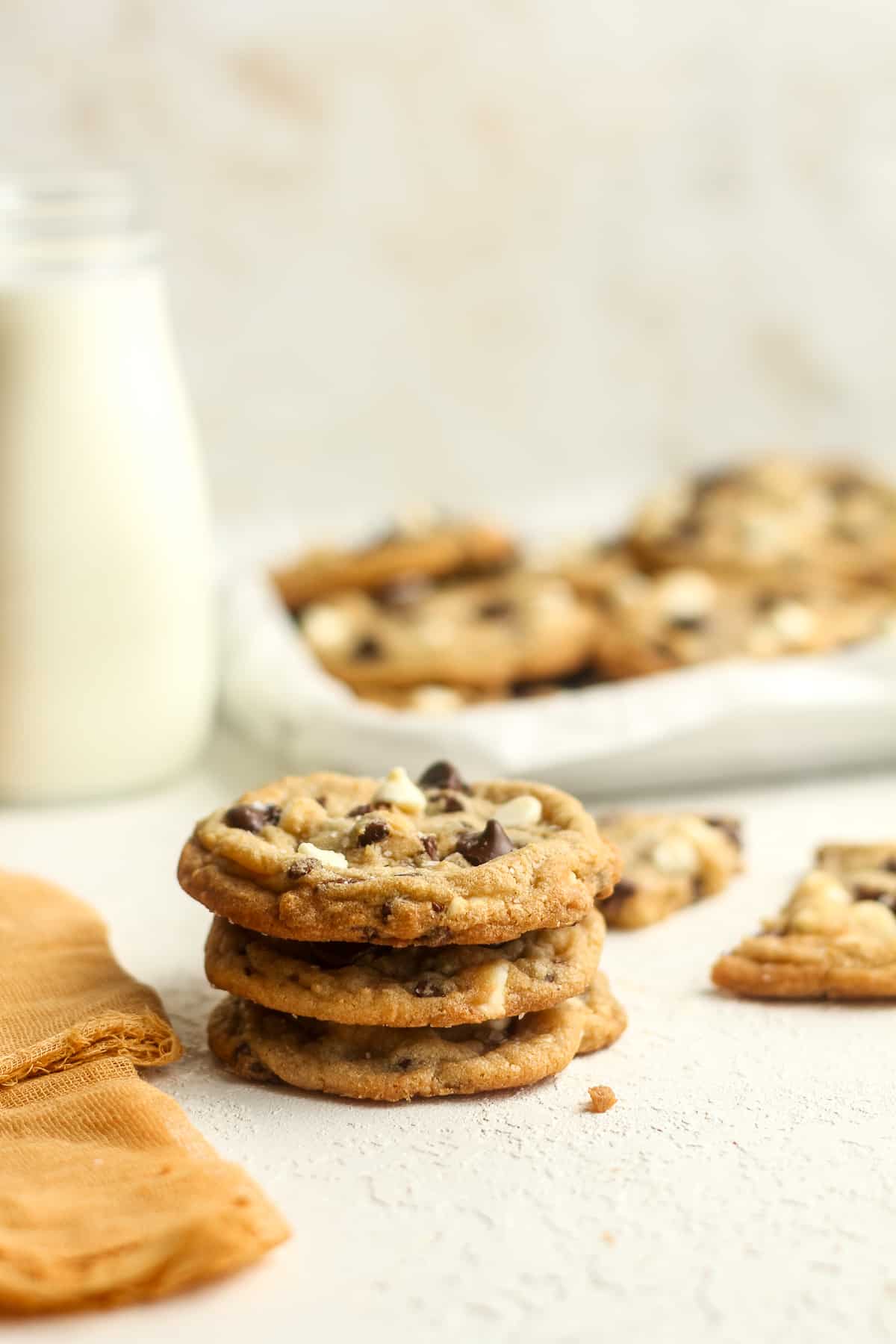 A stack of three thick cookies with a tray of cookies in the background.