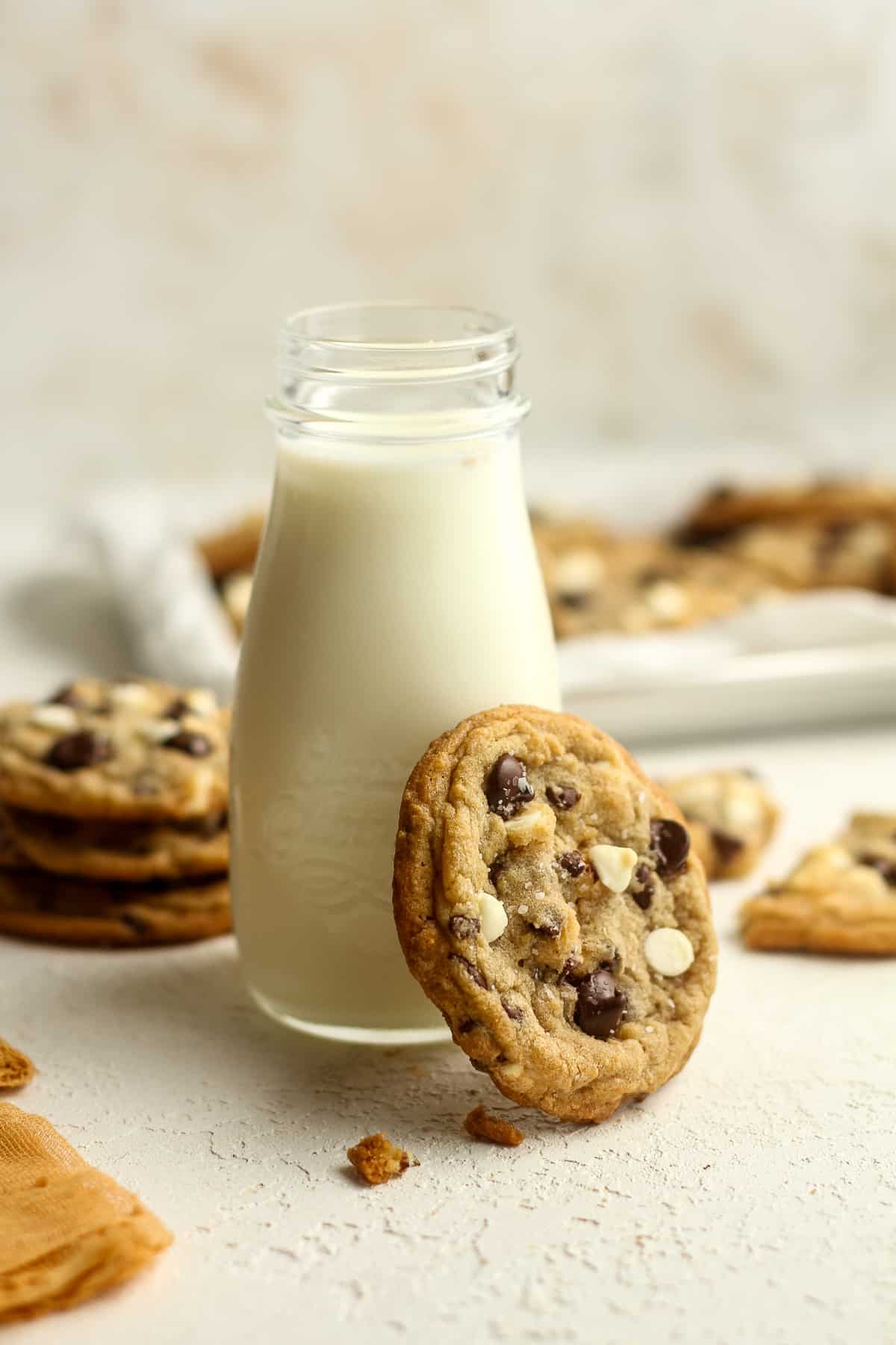 A chocolate chip cookie leaning against a jar of milk.