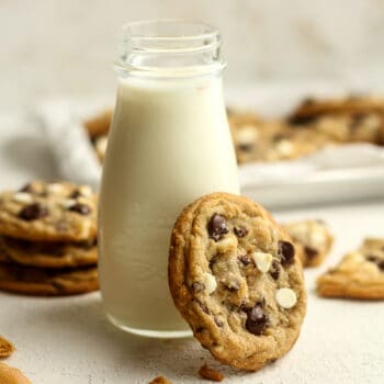 A cookie leaning against a jar of milk.