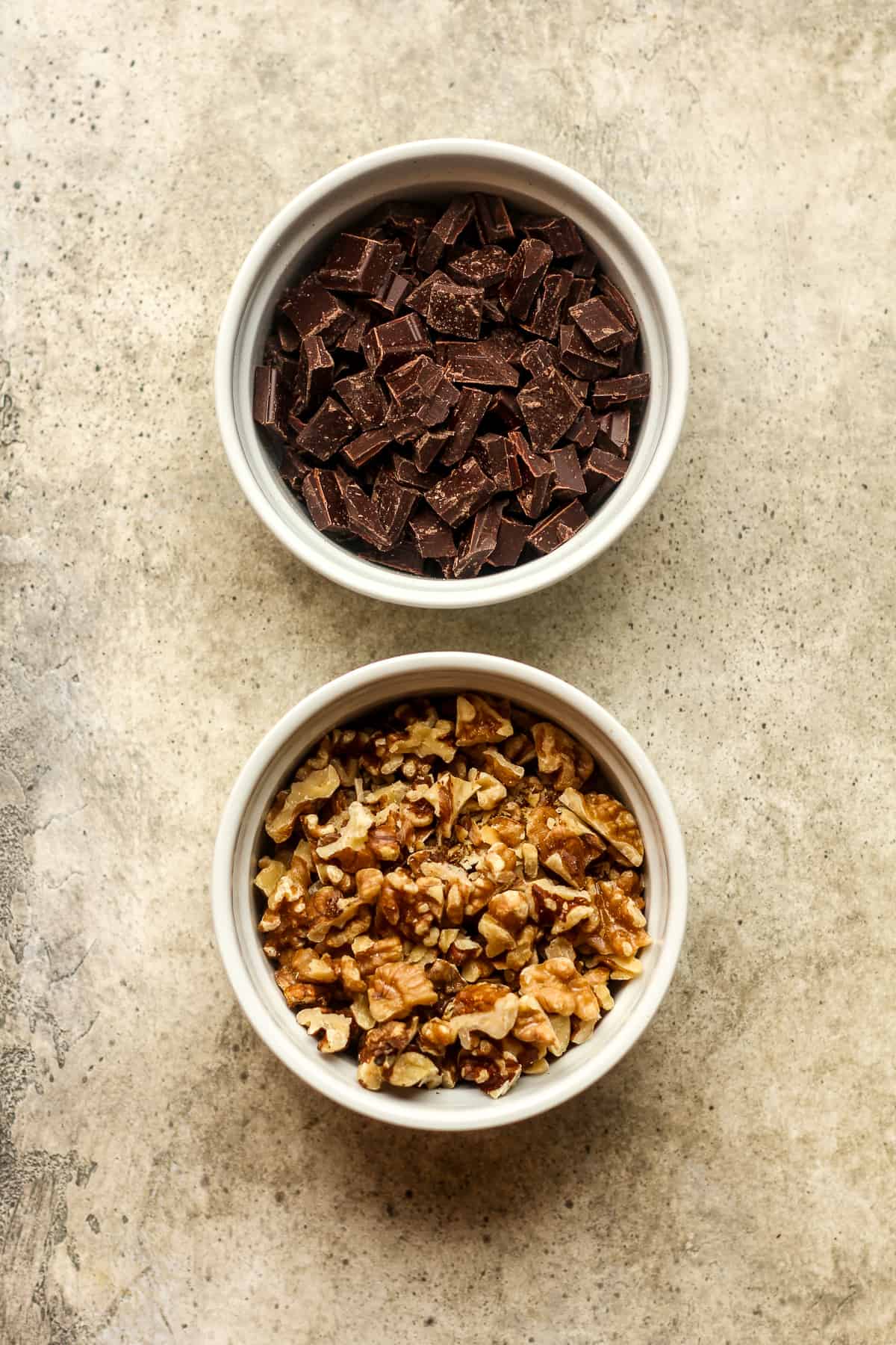 A bowl of chopped chocolate and a bowl of chopped walnuts.