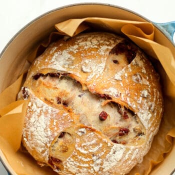 A Dutch oven with a loaf of baked cranberry walnut sourdough bread.
