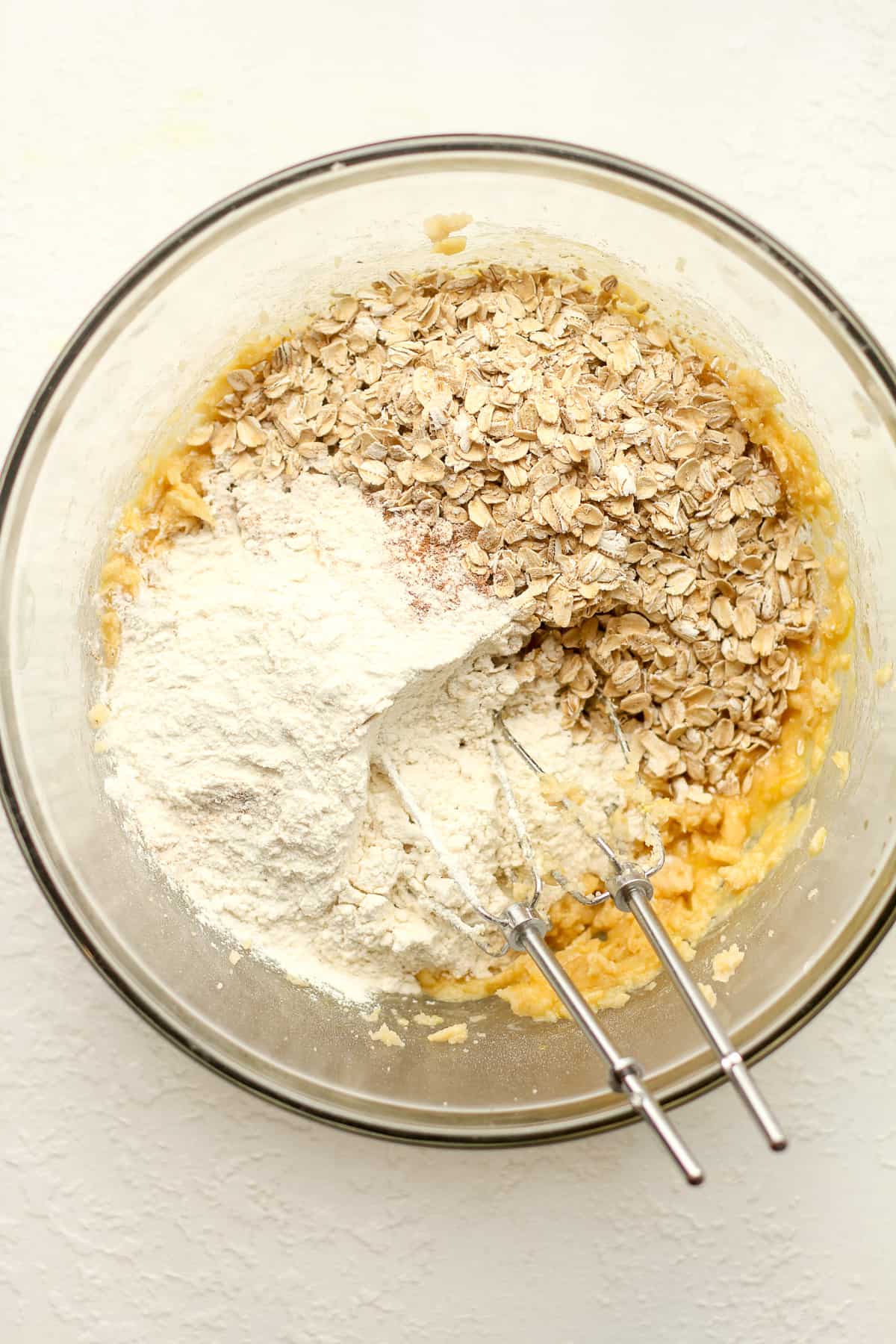 A bowl of wet ingredients with the oatmeal and flour on top.