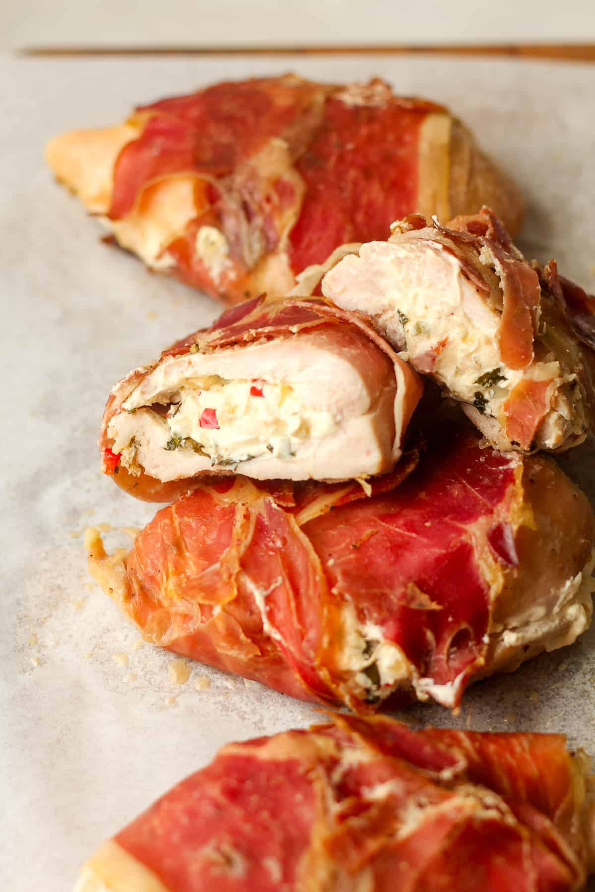 A tray of parma ham wrapped chicken and one halved showing the insides.