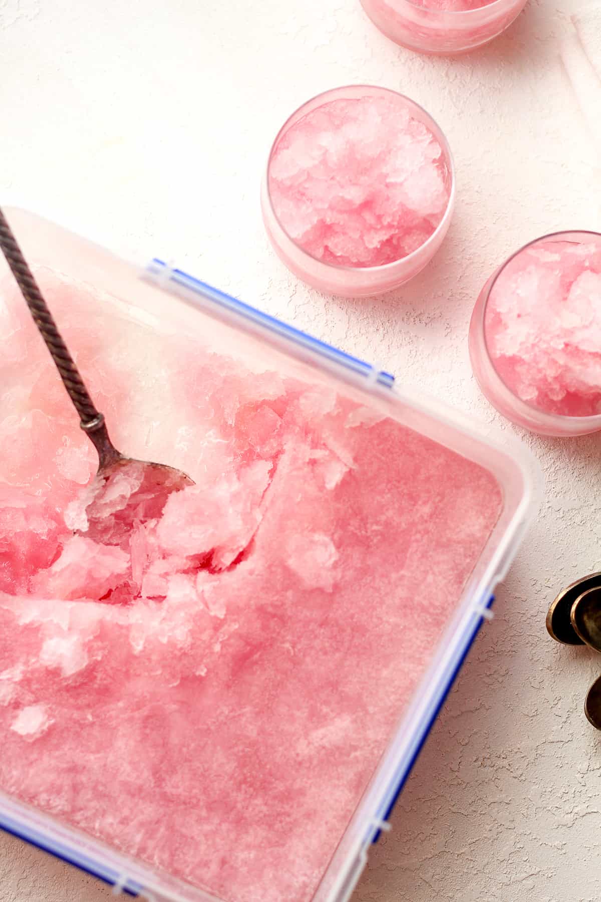 A container of pink slush with two glasses beside it.