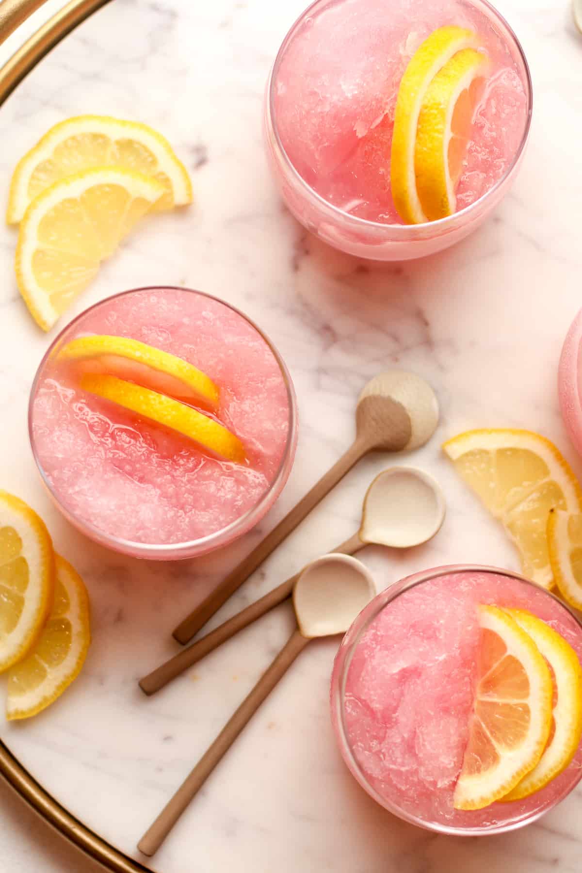 A tray of pink lemonade vodka slush cocktails with lemon slices.