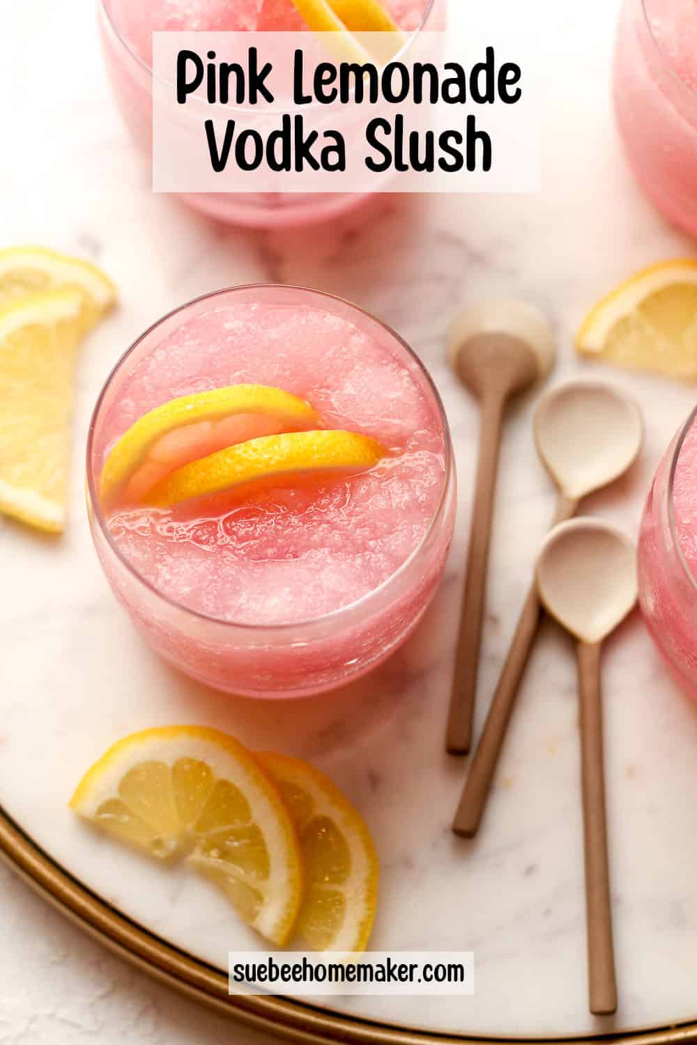 Overhead view of a tray of pink lemonade vodka slush drinks with lemon slices.