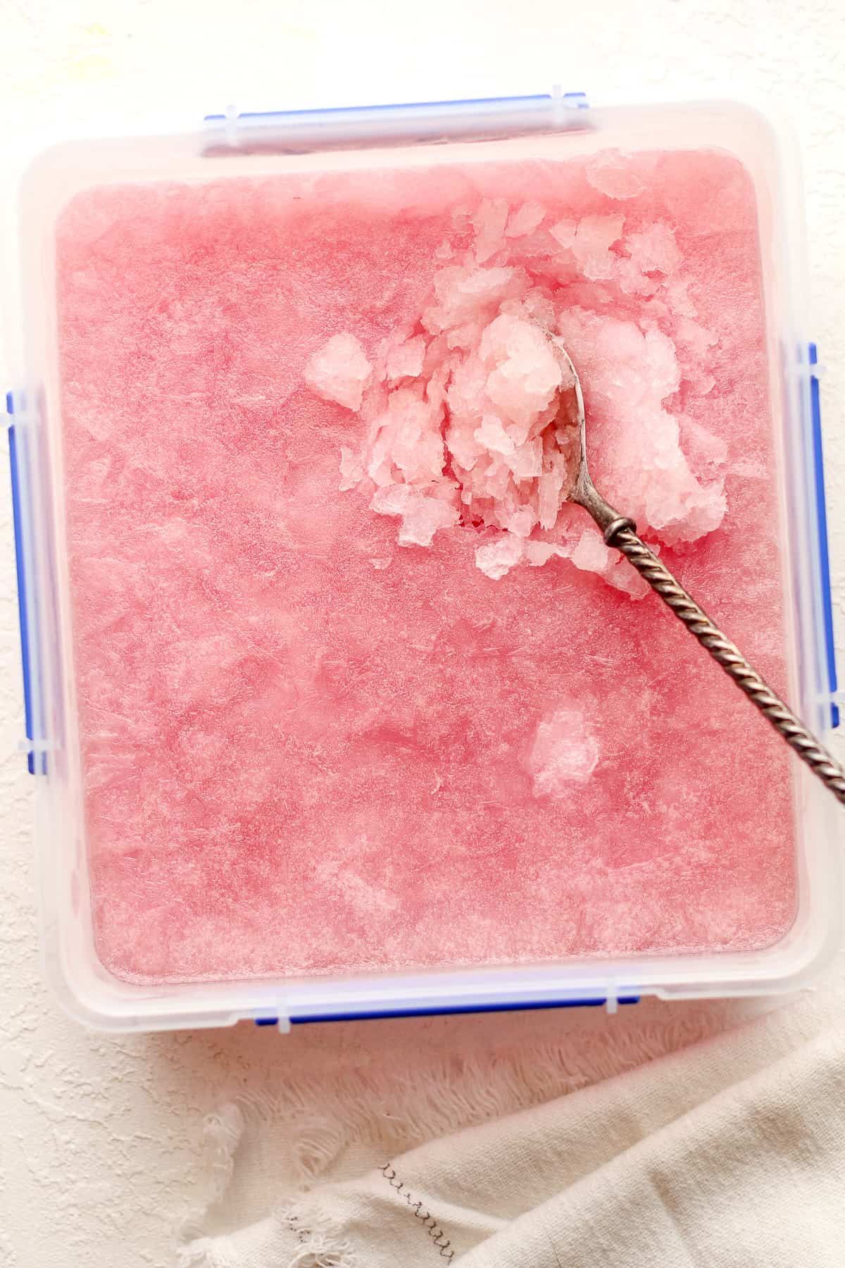 A container of frozen pink vodka lemonade slush with a spoon inside.