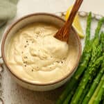 Closeup on a bowl of wasabi aioli on a plate with asparagus.