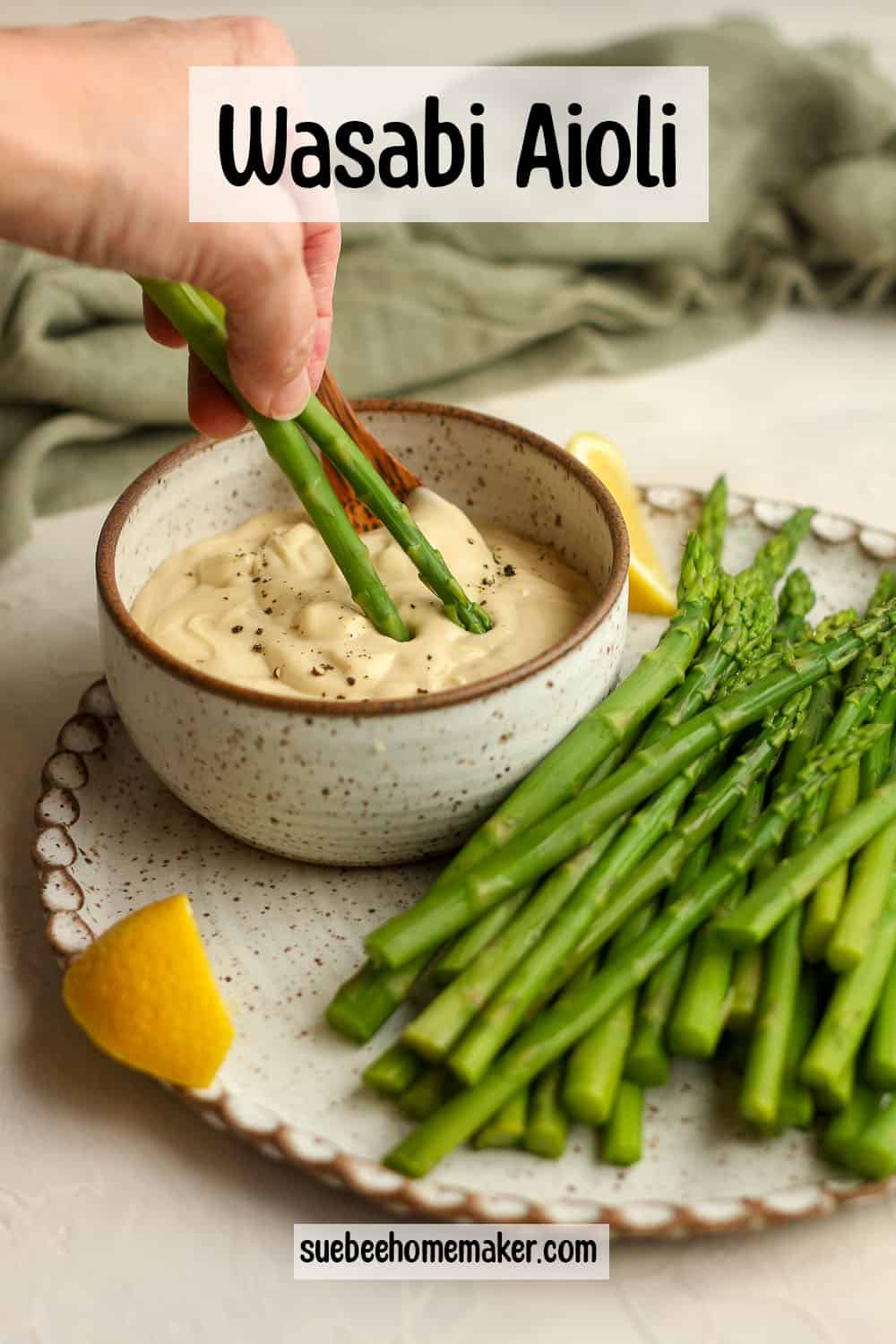 A hand dipping the blanched asparagus in the wasabi dip.