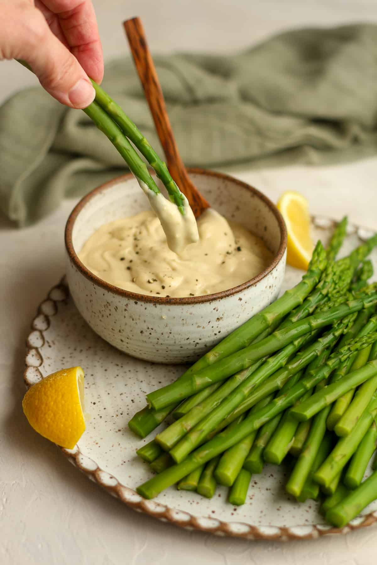 A hand dipping two stalks of asparagus in wasabi aioli.