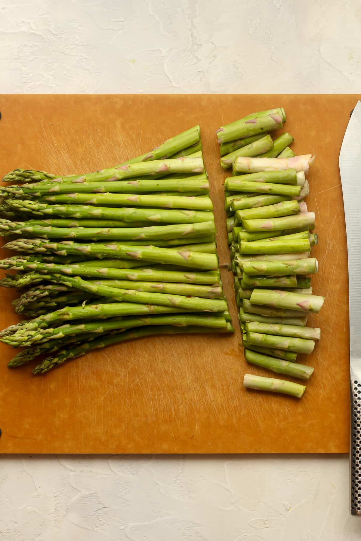 A cutting board of asparagus with the ends cut off.