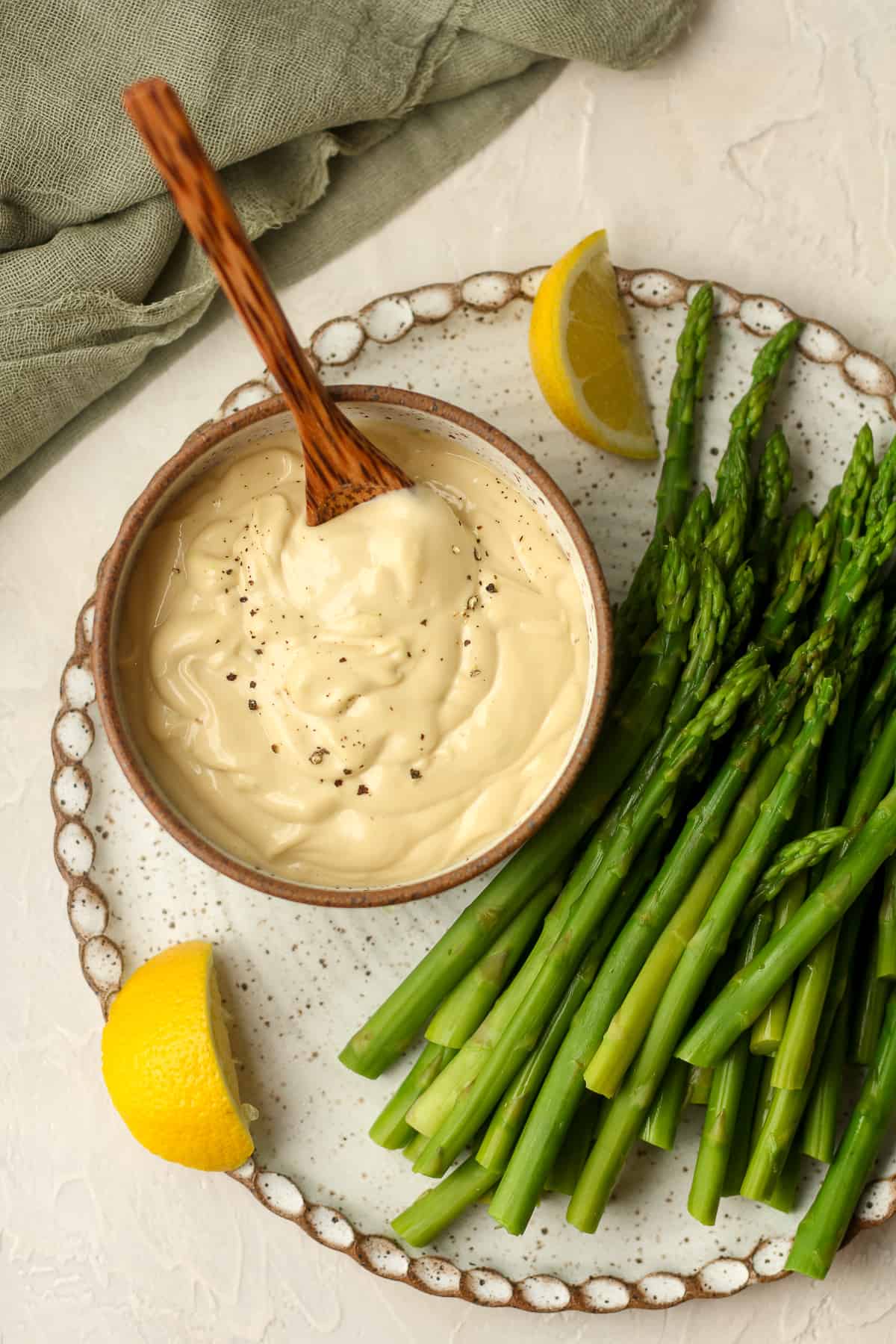 Overhead view of a plate of blanched asparagus with a bowl of wasabi aioli.