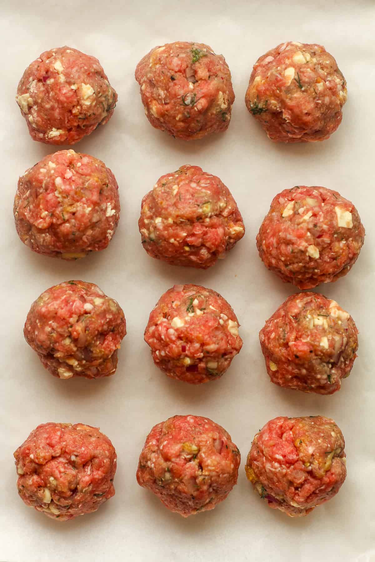 12 raw lamb meatballs on parchment paper.