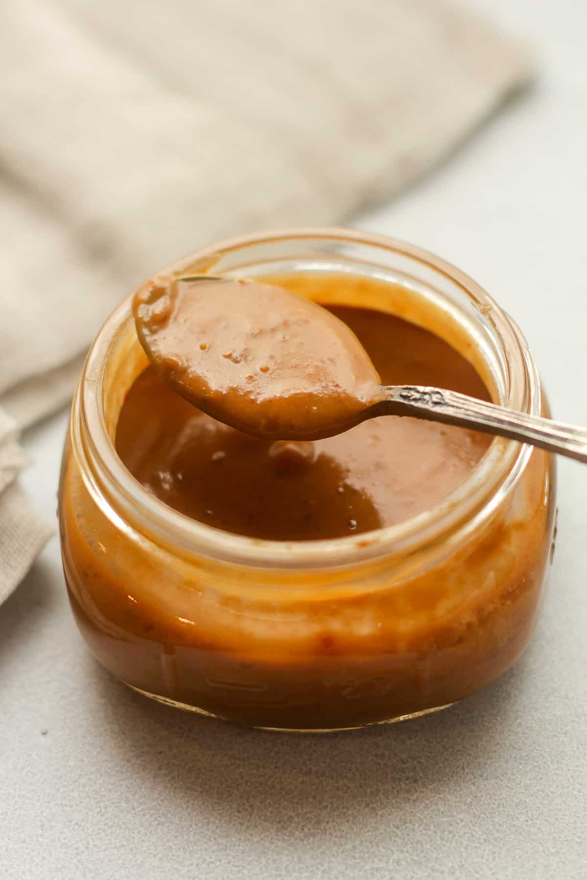 Side view of a short jar of peanut sauce with a spoonful on top.