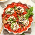 A dish of roasted tomatoes with warm burrata and drizzles of balsamic glaze.