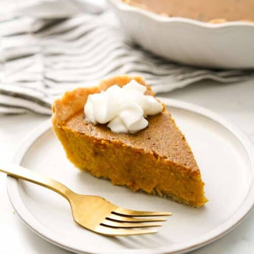 A slice of pumpkin pie with condensed milk on a small plate.