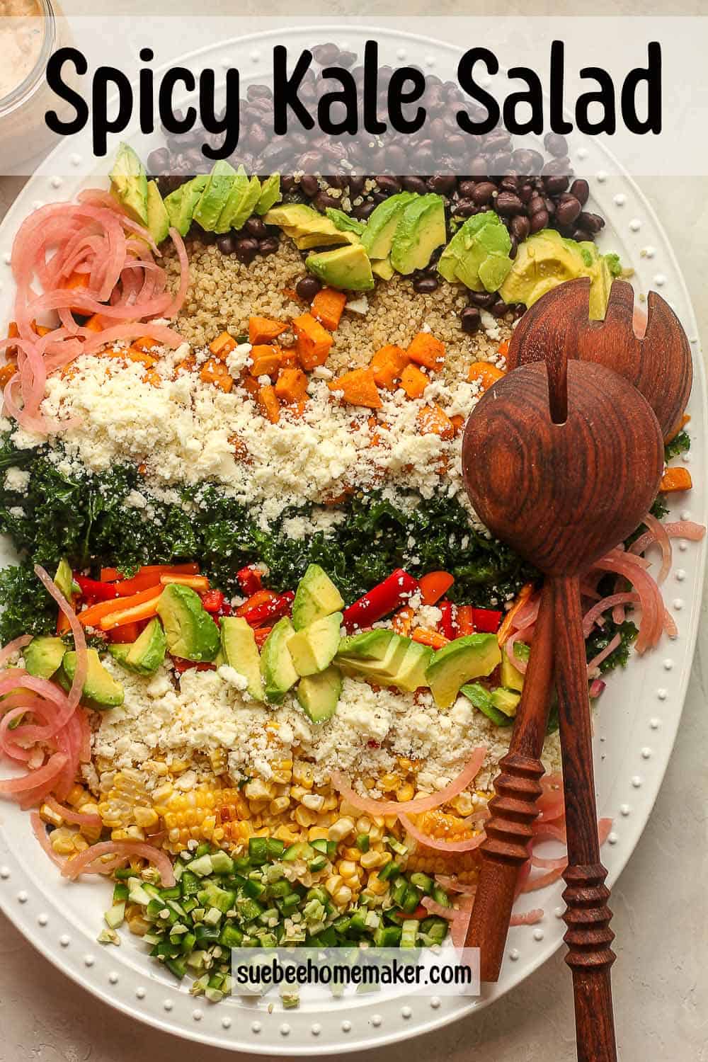 An oblong tray of a spicy kale salad with wooden spoons.