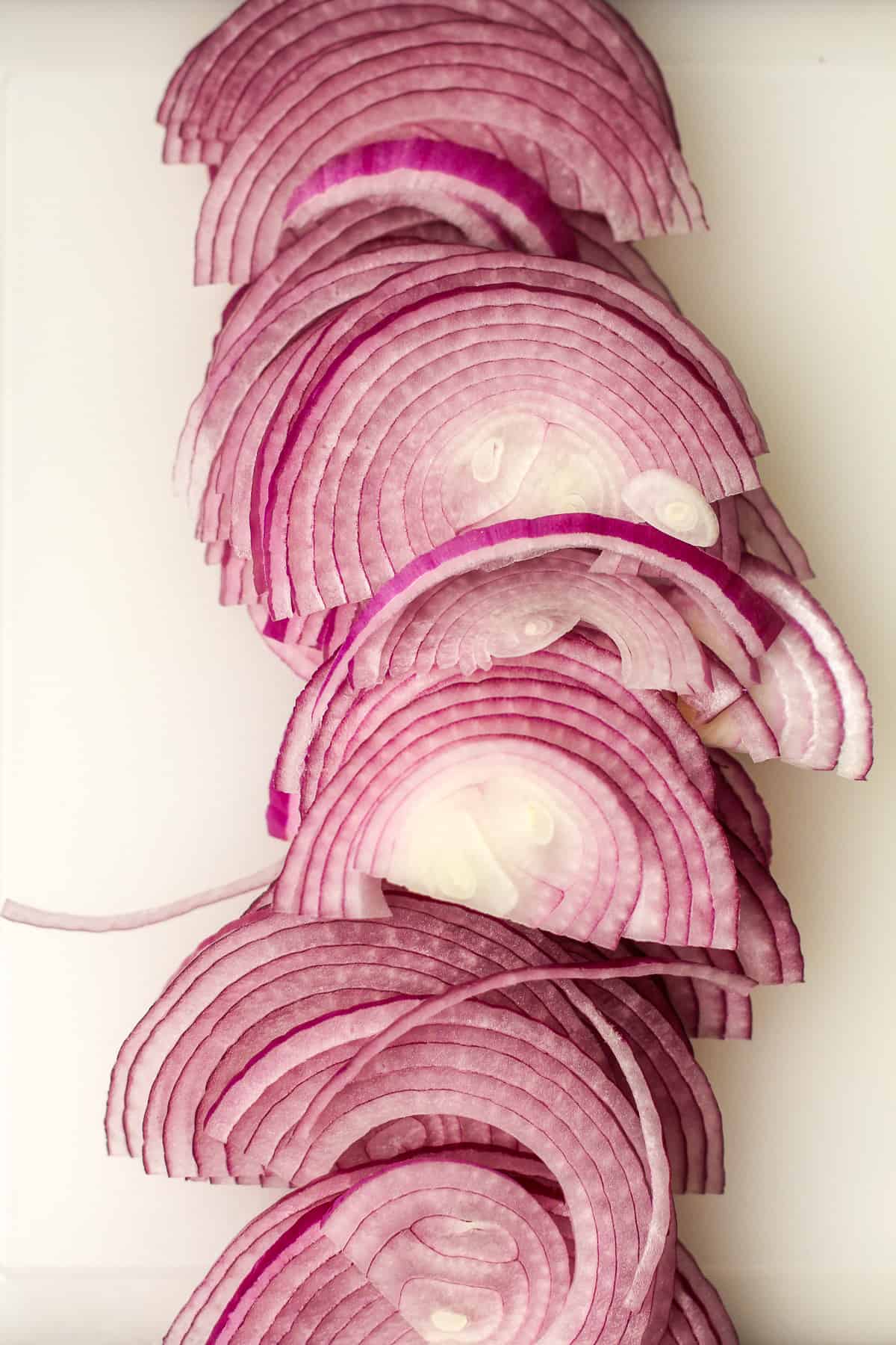 The thinly sliced red onion on a cutting board.