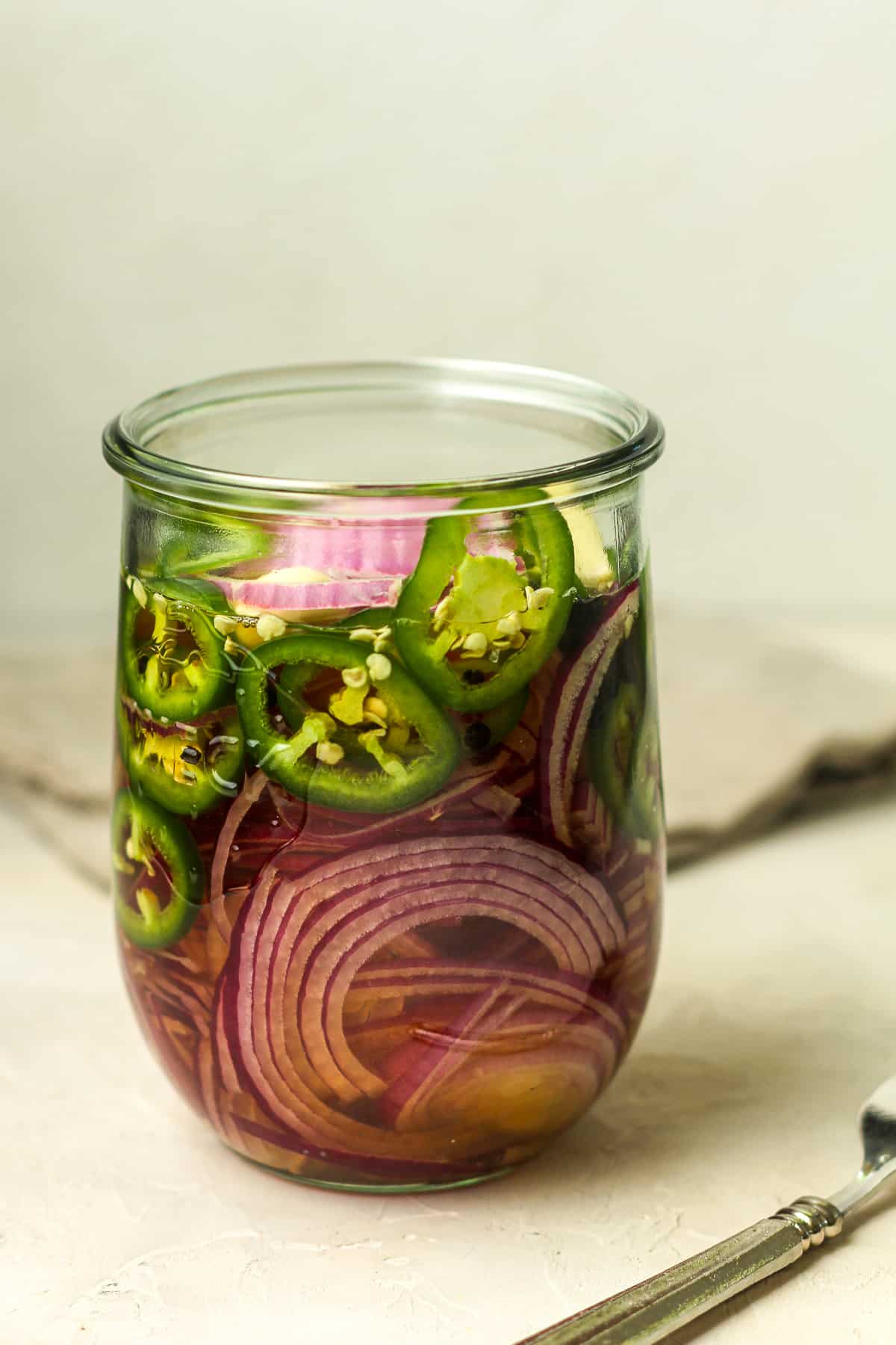 Side view of a jar of spicy pickled red onions and jalapenos.