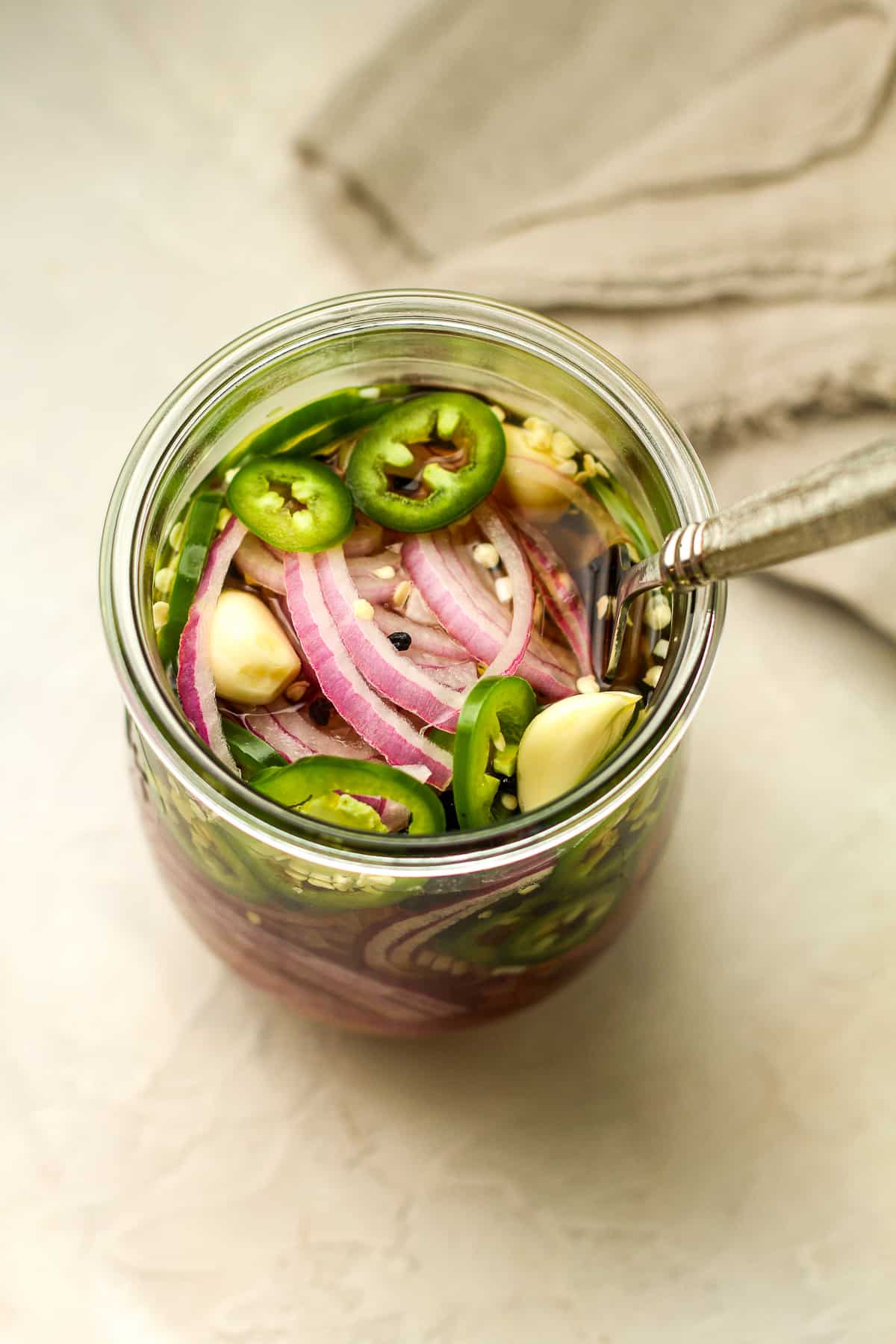 Overhead view of pickled red onions with jalapeno in a jar of brine.