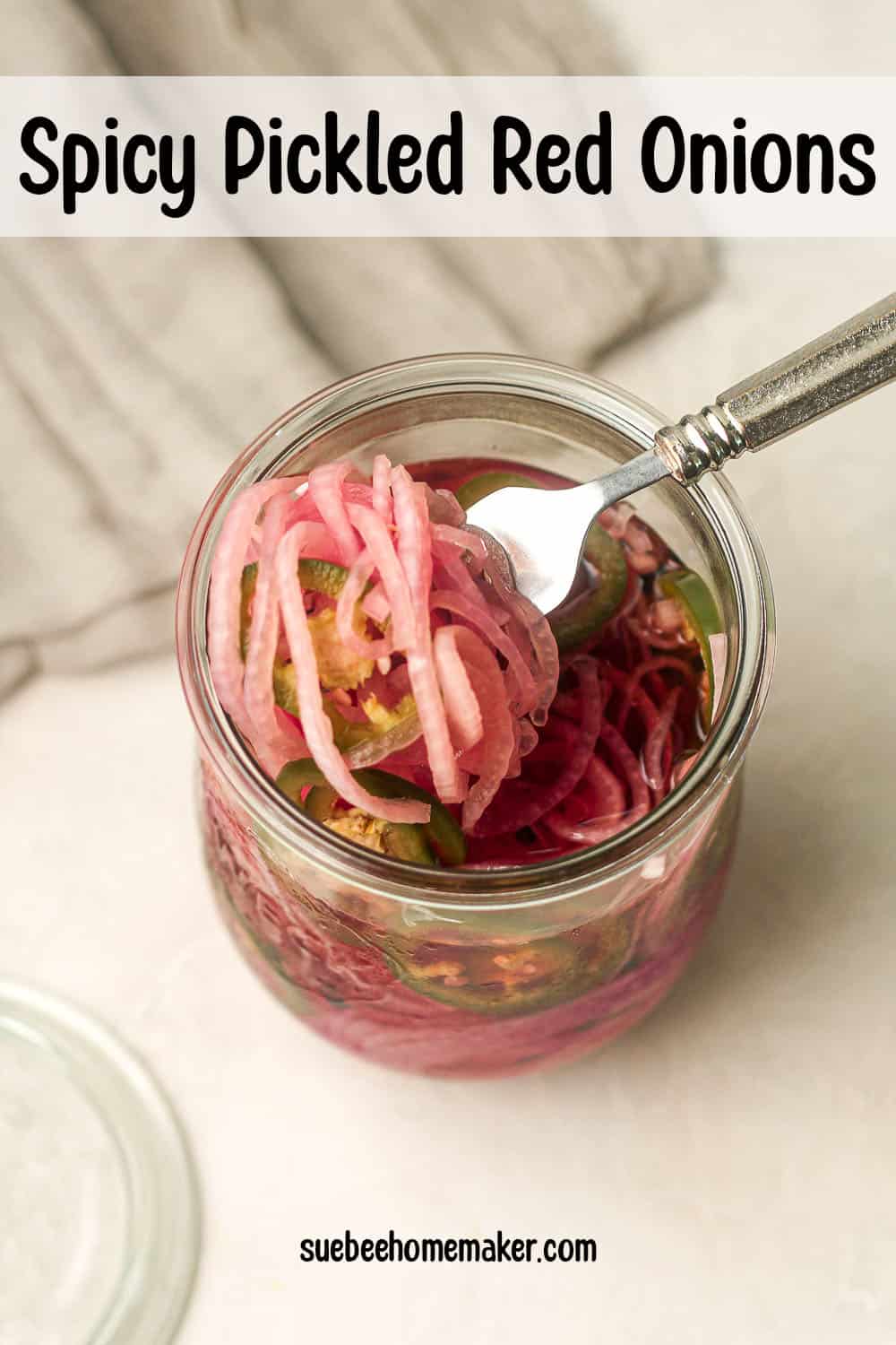 Overhead view of a large jar of spicy pickled red onions with a fork lifting some out.